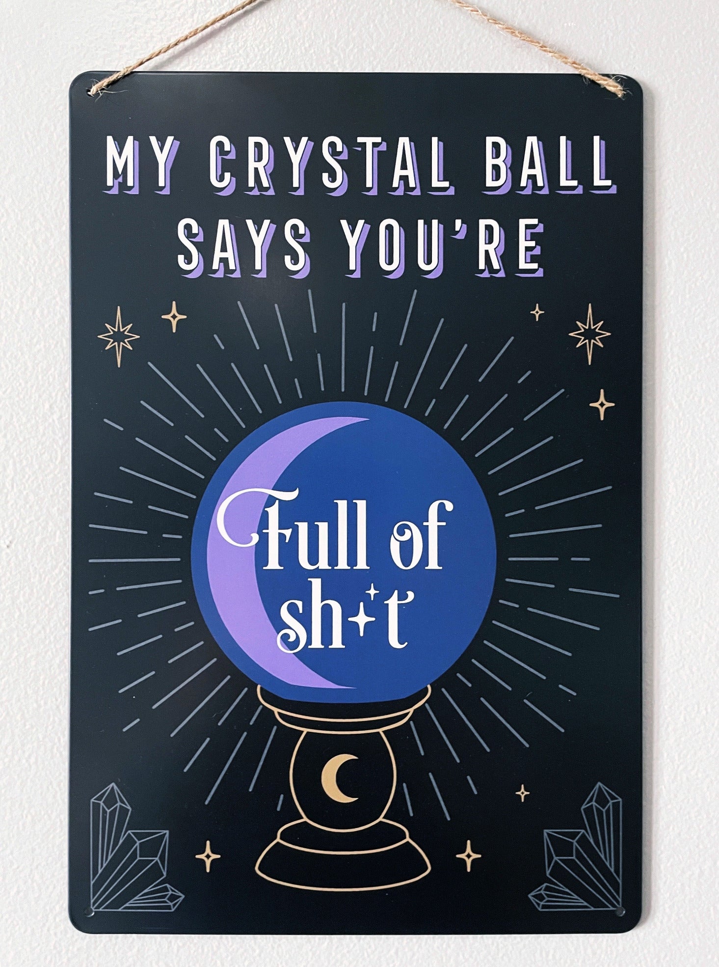 An image of a metal wall sign featuring a crystal ball design with the phrase "My crystal ball says you're full of shit" written in bold letters. The crystal ball design is illustrated in white against a deep purple background, with intricate lines and details that create a mystical and magical look.