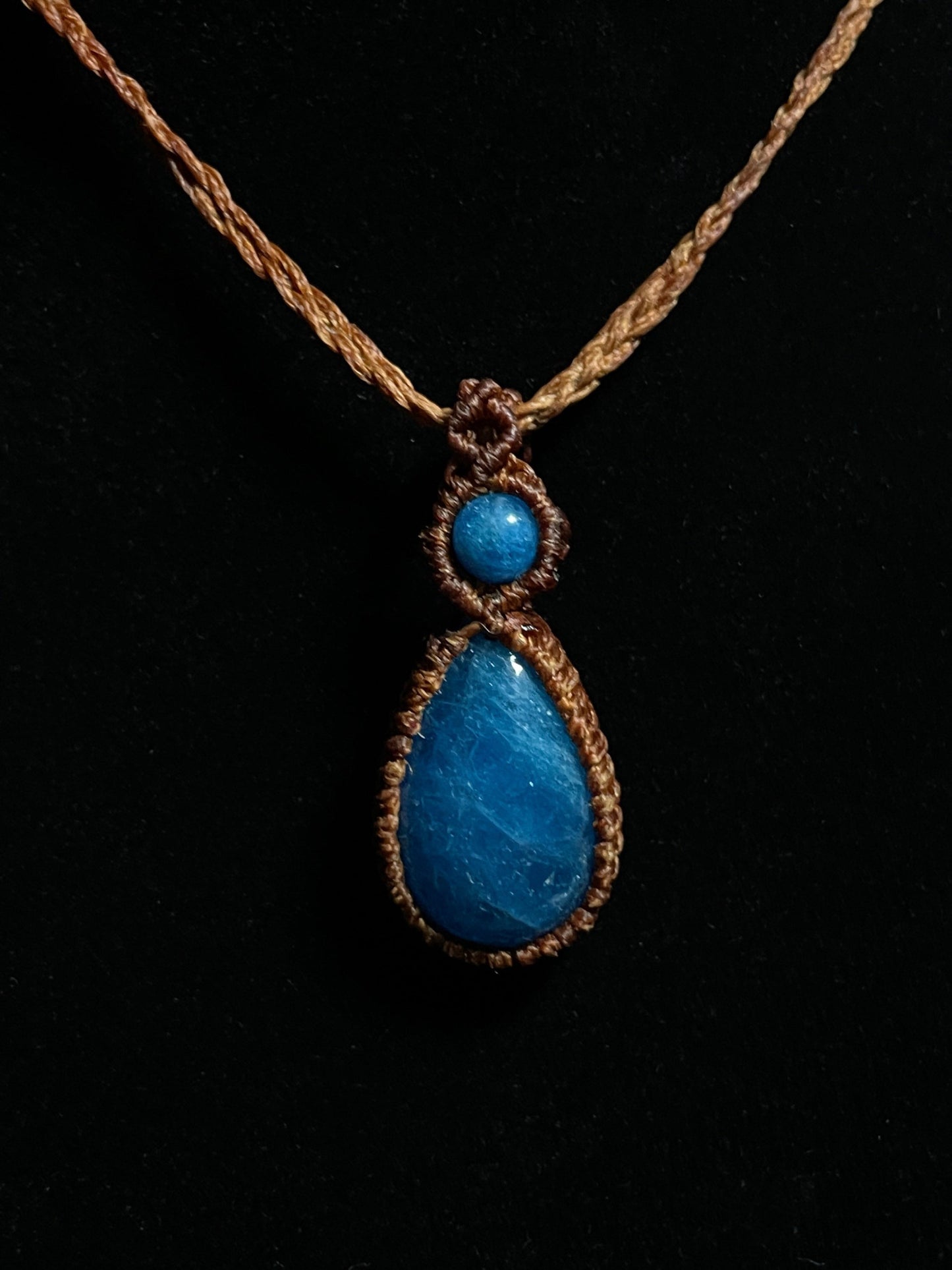 Pictured is a blue apatite cabochon wrapped in macrame thread. A gothic book and flowers are nearby.