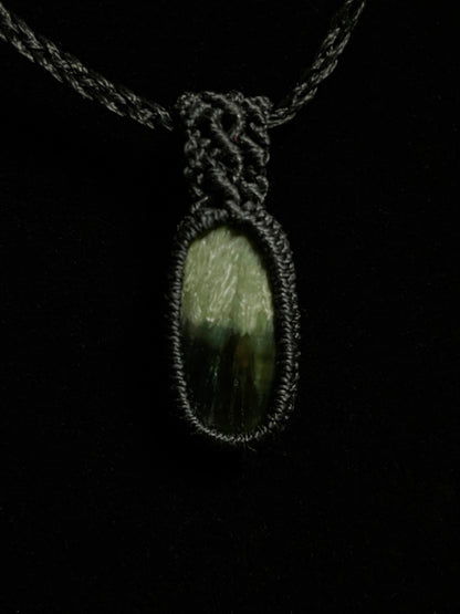 Pictured is a seraphinite cabochon wrapped in macrame thread. A gothic book and flowers are nearby.