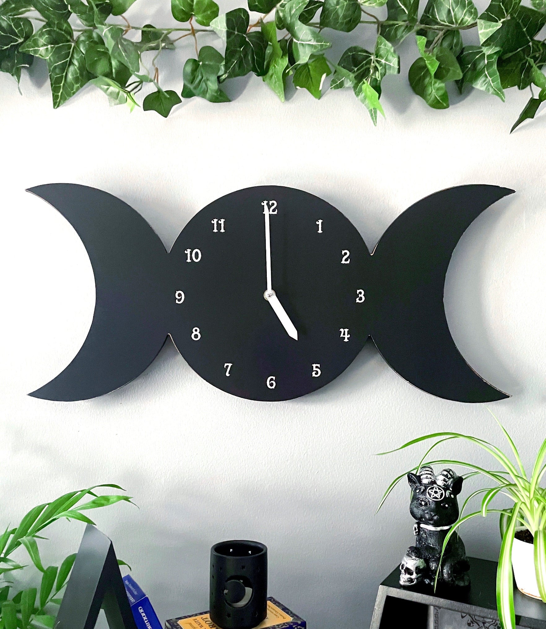 Pictured is a wall clock in the shape of a triple moon with the moon phases on it.